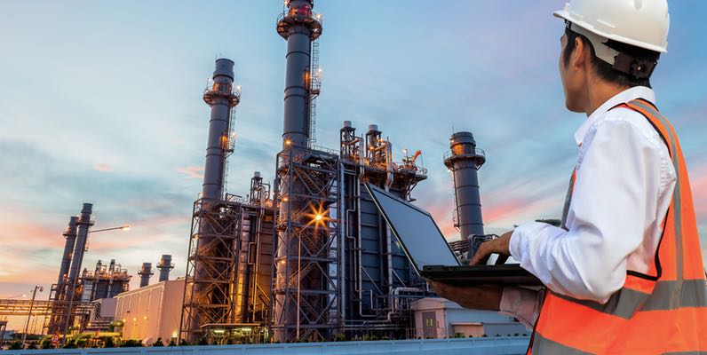 Engineering is use notebook check and standing in front of oil refinery building structure in heavy petrochemical industry